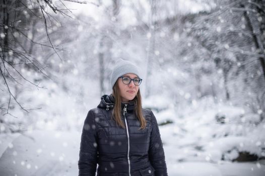 Woman in winter jacket walking in snowy winter forest, snowy winter day