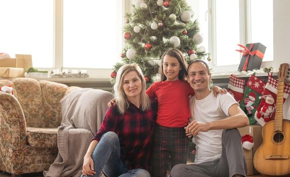 Merry Christmas and Happy New Year. Happy family is waiting for the New Year while sitting near beautiful Christmas tree at home.