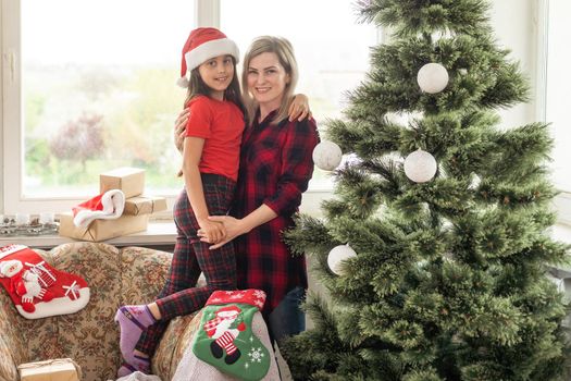 Mother and children decorating the house hang Christmas tree toys on the Christmas tree in a large wooden house.