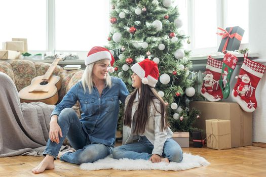 Merry Christmas and Happy Holidays. Cheerful mother and her cute daughter girl exchanging gifts. Mom and little child having fun near tree indoors. Loving family with presents in room.