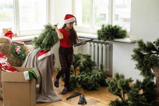 winter holidays and people concept - little girl makes an artificial Christmas tree.