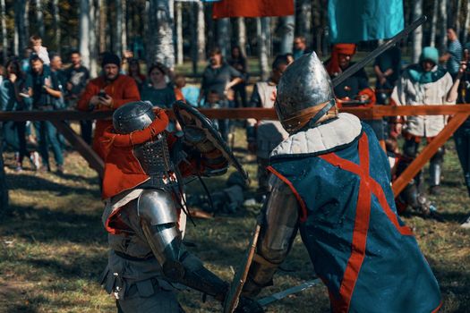 Two warriors in medieval costumes and with shields fight with swords. Reconstruction of historical jousting tournaments. Festival of medieval culture in park. Bishkek, Kyrgyzstan - October 13, 2019