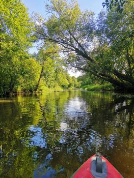 Kayaking on the river. Picturesque view of the banks overgrown with grass and trees. The nose of kayak. Rafting