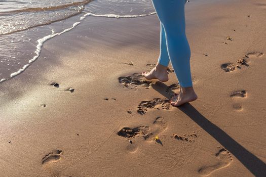 Close up woman legs walking on tropical sunset beach with smooth wave and bokeh sun light wave abstract background. Travel vacation and freedom feel good concept. Vintage tone filter color style