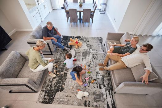 Big family in living room home with parents, baby or children play on carpet for growth, development and wellness. Overhead grandmother and grandfather talking to kids for language learning in lounge.