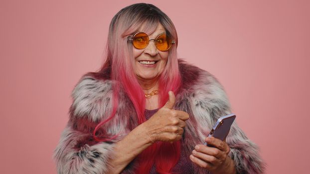 Lovely tourist senior woman using smartphone typing new post on web, browsing, searching, addiction of social networks, show thumbs up like, positive feedback, recommends wifi cellular connection 5G