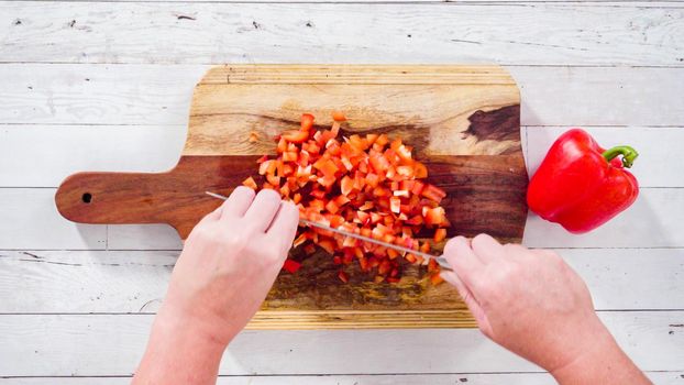 Flat lay. Mincing organic red bell peppers on a wood cutting board.