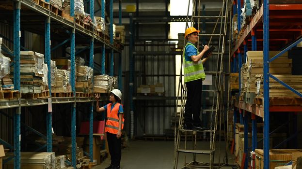 Warehouse workers in safety uniform working in warehouse full of tall shelves with goods in cardboard boxes.
