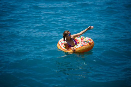 Beautiful young woman fell from an inflatable circle into the blue sea. Girl on vacation swims with a circle on the sea