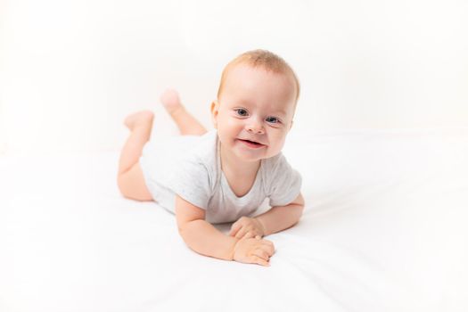 The baby lies on a white background and smiles at the camera . Advertising of children's goods. A child on a white background. Happy baby. The smile of a child. Children 's article . copy space