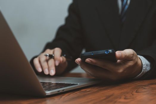 Businessman working with smartphone in his hands and computer laptop on desk.