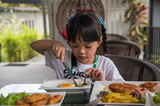 little girl asian eat fried egg on dish at table.