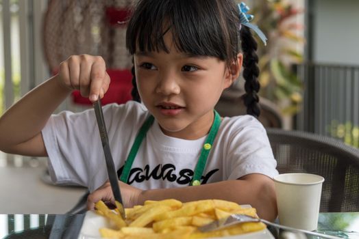 Young Asian girl eating french fries young kid fun happy potato fast food.