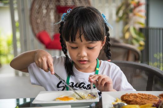 little girl asian eat fried egg on dish at table.