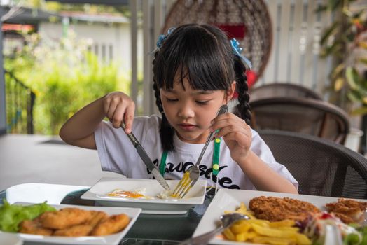 little girl asian eat fried egg on dish at table.