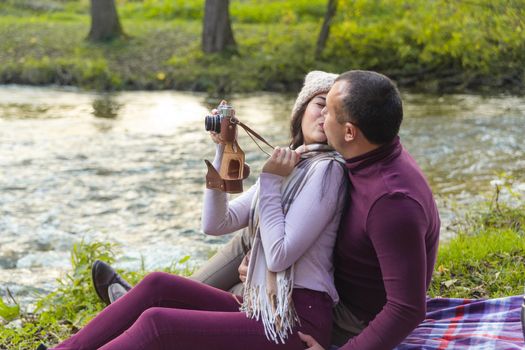 A happy couple on a picnic by the river is photographed for memory.