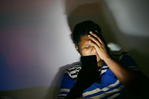 young man sitting on bed using smart phone at night .