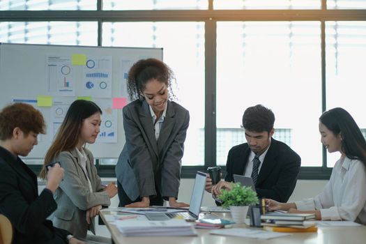 Asian business woman leader in a meeting with her multi-ethnic colleagues at the office presenting sales data or forecast for a project.