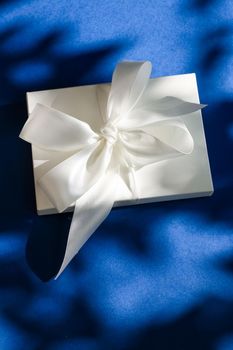 Anniversary celebration, shop sale promotion and bridal surprise concept - Luxury holiday white gift box with silk ribbon and bow on blue background, luxe wedding or birthday present