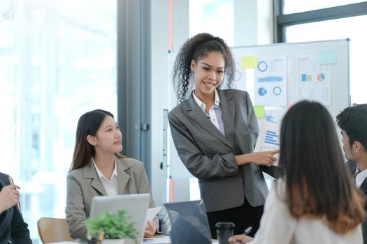 Asian business woman leader in a meeting with her multi-ethnic colleagues at the office presenting sales data or forecast for a project.