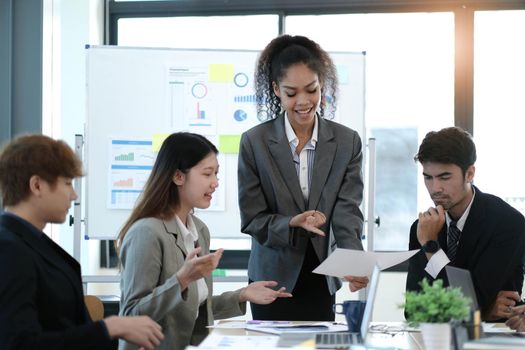 Asian business woman leader in a meeting with her multi-ethnic colleagues at the office presenting sales data or forecast for a project.