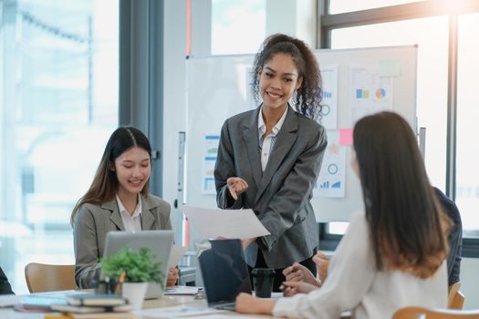 Asian business woman leader in a meeting with her multi-ethnic colleagues at the office presenting sales data or forecast for a project.