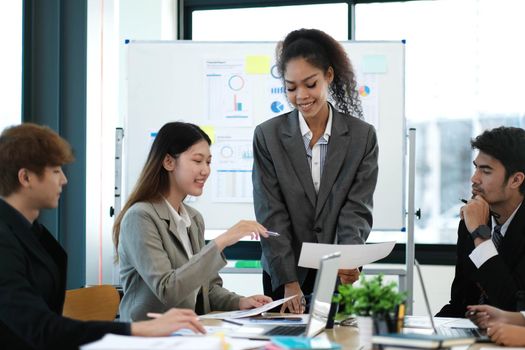 Asian business woman leader in a meeting with her multi-ethnic colleagues at the office presenting sales data or forecast for a project.