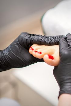 Foot massage with moisturizing and peeling cream by pedicurist hands wearing black gloves, close up