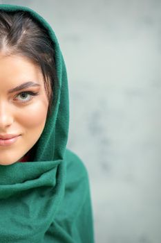 Portrait of a pretty young caucasian woman with makeup in a green headscarf on gray background