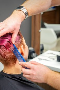 Hands of hairdresser combing hair making short pink hairstyle for a young caucasian woman in a beauty salon