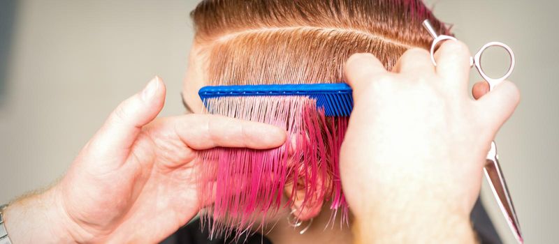 Hands of hairdresser combing hair making short pink hairstyle for a young caucasian woman in a beauty salon