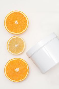 Flat lay composition of white jar with orange slices on white background, skincare cosmetics, top view