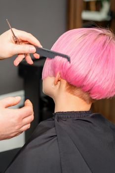 Hands of hairdresser combing hair making short pink hairstyle for a young caucasian woman in a beauty salon