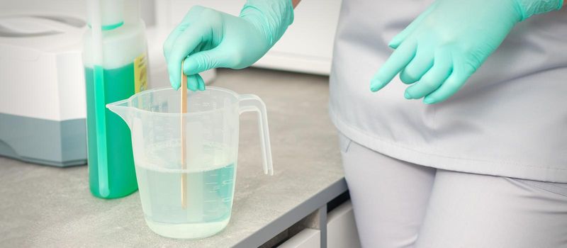 The beautician uses a stick to mix disinfectant into the water. Sterilization of tools