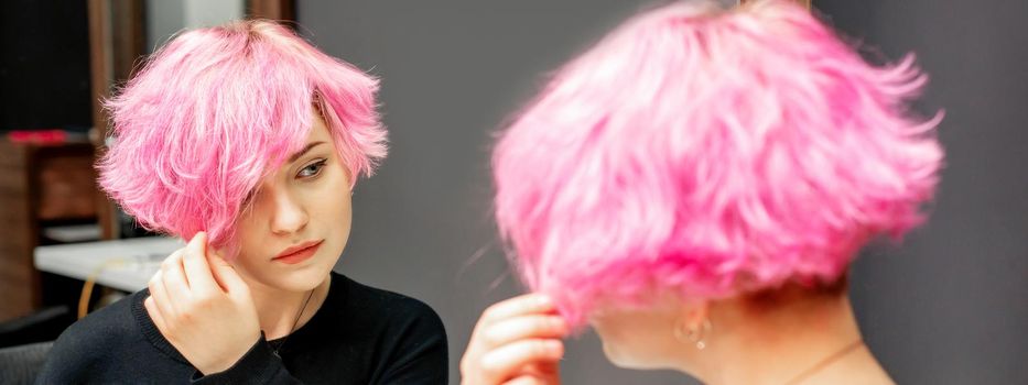 Beautiful young caucasian woman looking at her short pink hair in a mirror