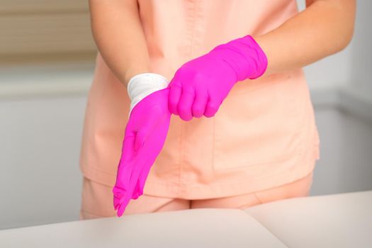 Hand of beautician puts on sterile pink gloves prepares to receive clients indoors