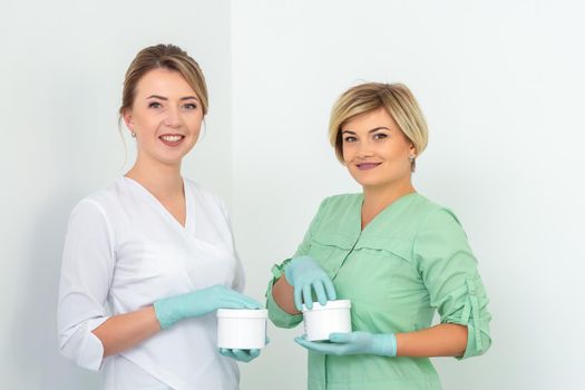 Two cosmeticians with jars of wax for depilation smiling against a white background. Natural product for hair removal. Copy space