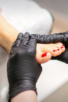 Foot massage with moisturizing and peeling cream by pedicurist hands wearing black gloves, close up