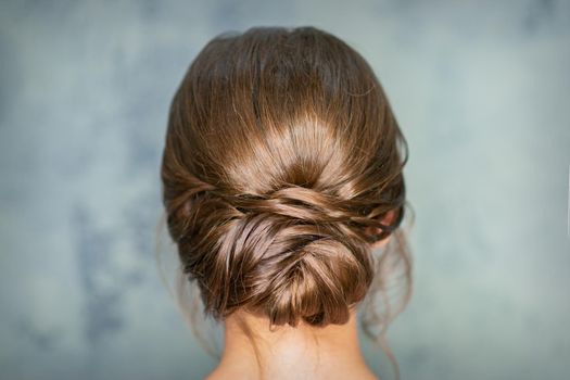 Rearview of young brunette woman with beautiful middle bun hairstyle on gray background