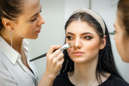 Closeup portrait of a woman applying dry cosmetic tonal foundation on the face using a makeup brush. Makeup detail