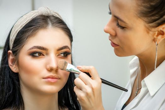 Closeup portrait of a woman applying dry cosmetic tonal foundation on the face using a makeup brush. Makeup detail