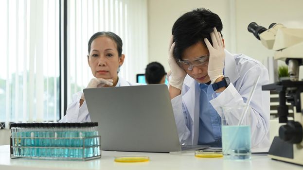 Professional scientists wearing white coats conducting experiment in research laboratory. Scientific research and technology concept.