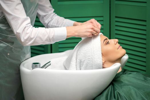 A hairdresser is wrapping a female head in a towel after washing hair in the beauty salon
