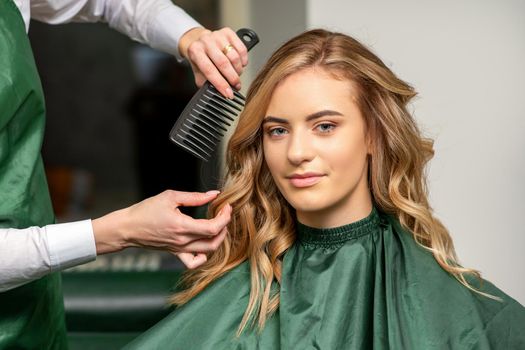 Hairdresser making hairstyling for the woman while combing with hairbrush, comb in a hair salon