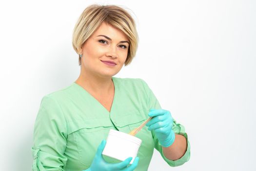 Cosmetician holding a jar of wax for depilation smiling on a white background. Natural product for hair removal. Copy space