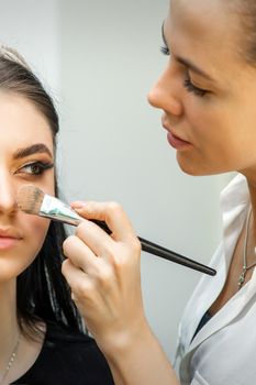 Closeup portrait of a woman applying dry cosmetic tonal foundation on the face using a makeup brush. Makeup detail