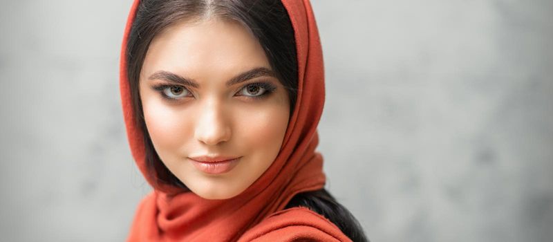 Portrait of a pretty young caucasian woman with makeup in a red headscarf on gray background