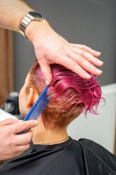 Hands of hairdresser combing hair making short pink hairstyle for a young caucasian woman in a beauty salon