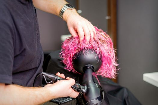 Hair Stylist making hairstyle using hair dryer blowing on wet custom pink hair at a beauty salon