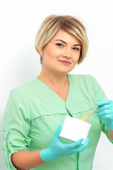 Cosmetician holding a jar of wax for depilation smiling on a white background. Natural product for hair removal. Copy space